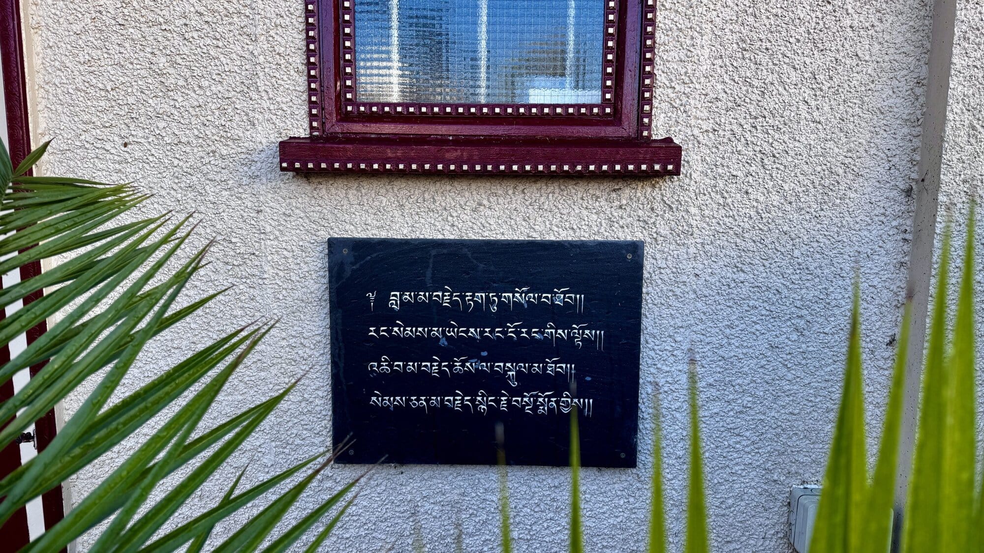 A dark slate plaque with Tibetan script engraved in white, mounted on the textured cream-coloured exterior wall of the Sakya Thubten Ling centre in Bournemouth.